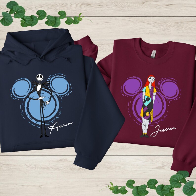 two sweatshirts with cartoon characters from the movie " jack Skellington and Sally Ann". The sweatshirt on the left is a navy blue hoodie with a skeleton and a mouse, while the sweatshirt on the right is a burgundy long-sleeved shirt with a girl and a mouse.