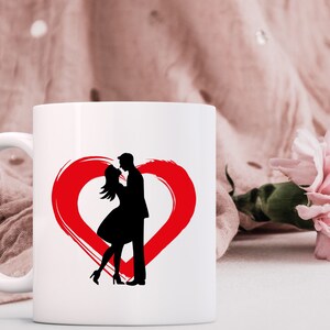 May include: White ceramic mug with a red heart design and a silhouette of a couple kissing inside the heart.