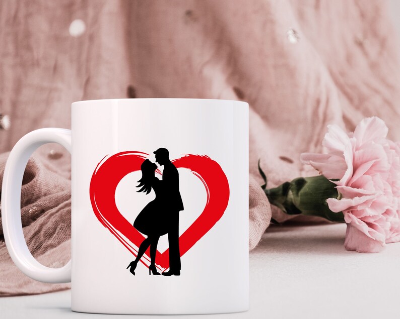 May include: White ceramic mug with a red heart design and a silhouette of a couple kissing inside the heart.