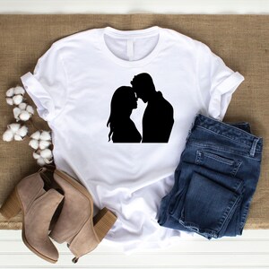May include: White t-shirt with a black silhouette of a couple embracing.