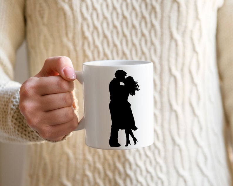 May include: White ceramic mug with a black silhouette of a couple kissing. The mug has a handle on the right side.