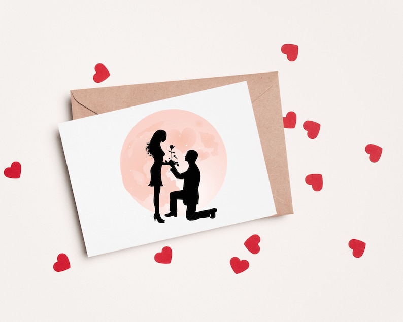May include: A white card with a silhouette of a couple in love. The man is kneeling and holding a rose, while the woman is standing and smiling. The background is a pink circle, resembling a moon.