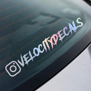 May include: A holographic decal with the text "VELOCITYDECALS" in a stylized, jagged font, along with the Instagram logo. The decal is designed to be applied to a car window.