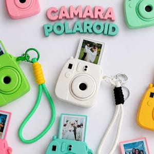 May include: A collection of miniature camera keychains in various pastel and bright colors, including white, pink, yellow, green, and purple. Each keychain features a small photo insert, a wrist strap, and a metal ring for attachment.