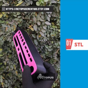 May include: A black and pink object with a grid-like design is held against a backdrop of green leaves. The object has a rectangular shape with a pink, open-grid design on one side. The text "01 STL" is on a white and red rectangle.