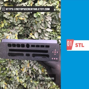May include: A black, rectangular 3D-printed object with various cut-out shapes and a series of small, pink buttons. The object is held against a backdrop of green foliage and a bright blue background. The text "01 STL" is visible.