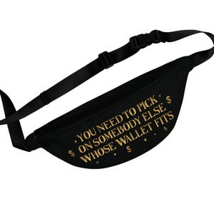 May include: Black fanny pack with a black adjustable strap and buckle. The bag features gold text that reads "YOU NEED TO PICK ON SOMEBODY ELSE WHOSE WALLET FITS" with dollar signs and star accents.