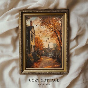 May include: A framed painting of a cozy cottage with a brick chimney and a path leading to it. The cottage is surrounded by trees with autumn leaves in shades of orange, yellow, and red. The painting has a gold frame and the text "COZY COTTAGE WALL ART" is printed below the frame.