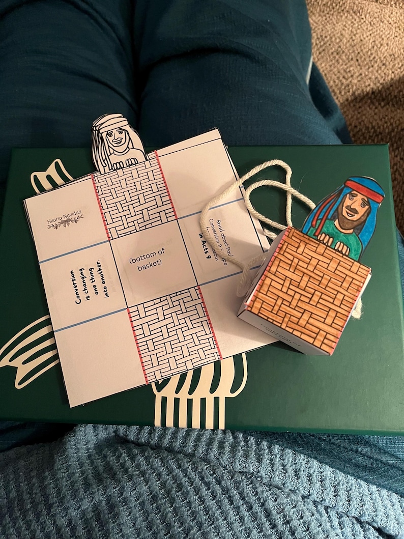 Peut inclure: Un artisanat en papier fait &agrave; la main repr&eacute;sentant une sc&egrave;ne biblique. L'artisanat pr&eacute;sente un panier et des personnages avec des visages illustr&eacute;s. Le texte sur le papier se lit "Conversion is changing one thing into another" et "Read about Paul Conversion in Acts 9."