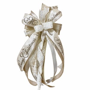 May include: A decorative Christmas bow in cream and gold. The bow features multiple layers of ribbon, with the words "Merry Christmas" in silver script. The bow is designed for holiday decorating.