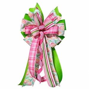 May include: A decorative bow featuring a mix of ribbons in various patterns and colors. The bow includes bright green, pink plaid, floral, and striped ribbons. The bow is suitable for decorating wreaths, gifts, or other crafts.