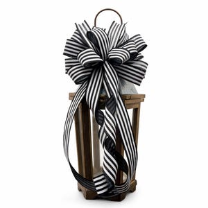 May include: A wooden lantern with a decorative black and white striped bow. The lantern has a metal handle and a hinged door. The bow is large and has long, flowing ribbons. The lantern is a decorative item.