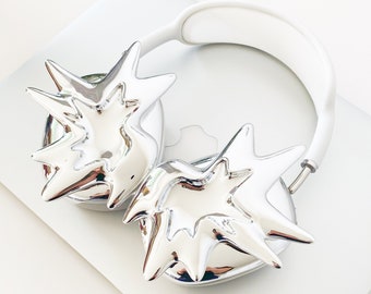 May include: Silver headphones with a unique starburst design on each earcup. The headphones have a white headband.