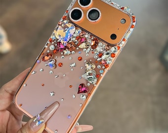 Puede incluir: Una funda transparente para teléfono con borde dorado rosa, adornada con una variedad de pedrería y cristales de colores. Los adornos incluyen formas de corazón, mariposa y estrella, creando un diseño glamuroso y llamativo.
