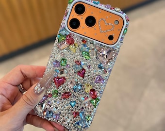 May include: A bedazzled phone case with a multitude of colorful rhinestones and gems. The case features an orange camera housing with a heart-shaped design. The case is encrusted with various shapes and sizes of rhinestones.