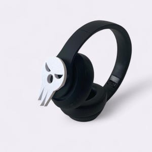 Peut inclure: Casque audio noir avec un embl&egrave;me de cr&acirc;ne blanc sur le c&ocirc;t&eacute;. Le casque est dot&eacute; d'un design de coussinet d'oreille rembourr&eacute; et d'une esth&eacute;tique &eacute;l&eacute;gante et moderne. L'embl&egrave;me de cr&acirc;ne ajoute une touche unique et audacieuse.