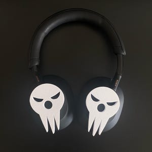 Op de afbeelding: Zwarte over-ear hoofdtelefoon met witte schedelvormige oorkapjes. Het schedelontwerp heeft een dreigende uitdrukking met twee ogen en een mond.