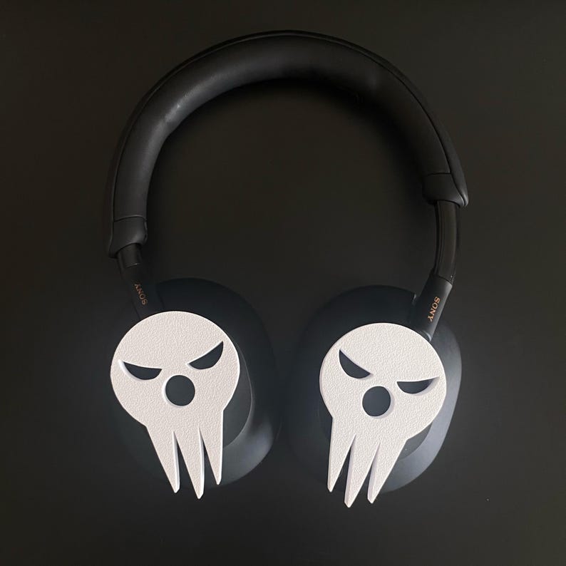 Op de afbeelding: Zwarte over-ear hoofdtelefoon met witte schedelvormige oorkapjes. Het schedelontwerp heeft een dreigende uitdrukking met twee ogen en een mond.