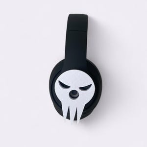 Peut inclure: Casque audio noir avec un motif de cr&acirc;ne blanc sur l'&eacute;couteur. Le cr&acirc;ne affiche une expression mena&ccedil;ante avec des sourcils anguleux et une m&acirc;choire pointue. Le casque a un bandeau rembourr&eacute;.