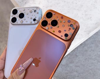 May include: Two decorative phone cases. One is silver with clear rhinestones, the other is copper with colorful rhinestones. Both cases have a glossy finish and feature the Apple logo.