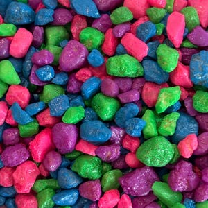 May include: A close-up of a variety of small, colorful, smooth, and shiny stones. The stones are in shades of pink, green, blue, and purple.