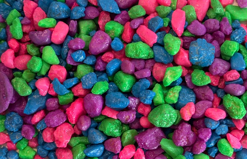 May include: A close-up of a variety of small, colorful, smooth, and shiny stones. The stones are in shades of pink, green, blue, and purple.