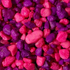 May include: A close-up of a pile of small pink and purple stones. The stones are smooth and have a glossy finish.