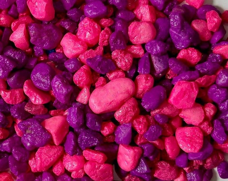 May include: A close-up of a pile of small pink and purple stones. The stones are smooth and have a glossy finish.