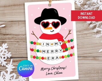 May include: A pink printable gift tag featuring a snowman wearing a black hat, red scarf, and sunglasses. The snowman is surrounded by a green and red beaded garland with gold stars and the words "In My Merry Era" spelled out in white letters.