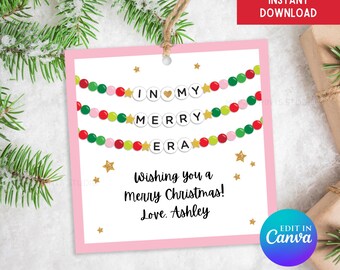 May include: Pink printable gift tag with a beaded garland spelling "I love my Merry Era" with gold stars. The tag also says "Wishing you a Merry Christmas! Love. Ashley" and "Edit in Canva".