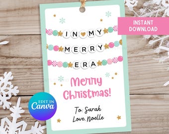 May include: A printable gift tag with a light blue background and pink and green decorations. The tag says "In My Merry Era" and "Merry Christmas!" with a pink heart. The tag is editable in Canva and includes the text "To: Sarah Love: Noelle".