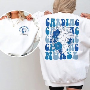 May include: White sweatshirt with a blue and white graphic of a heart with flowers and the text "CARDIAC NURSE". The front of the sweatshirt has the text "CARDIAC NURSE" in a smaller font.