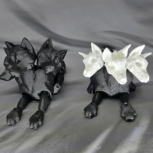 May include: Two three-headed wolf figurines, one black and one white. The black figurine is lying down with its heads facing forward, while the white figurine is lying down with its heads facing forward.