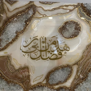 Op de afbeelding: Een abstract kunstwerk in wit en goud met een geode-ontwerp. De geode is gevuld met kleine, heldere kristallen en heeft een gouden omtrek. De Arabische kalligrafie "Subhanallah" is in goud op een witte achtergrond geschreven.