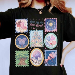 Peut inclure: T-shirt noir avec des motifs de timbres-poste color&eacute;s repr&eacute;sentant des images de parc &agrave; th&egrave;me. Les timbres incluent un ch&acirc;teau, une grande roue et Mickey Mouse. Le texte sur le t-shirt se lit "Meet Me On Main Street."