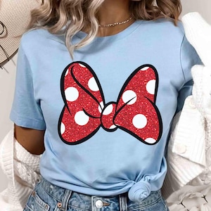 Puede incluir: Camiseta azul claro con un lazo rojo brillante con lunares blancos y contorno negro. El lazo est&aacute; centrado en la camiseta. La camiseta es de material suave y es adecuada para uso casual.