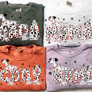 May include: Four crewneck sweatshirts in green, white, orange, and lavender. Each features a Dalmatian dog design with the words "DADA", "MAMA", "CODY", and "NAME" in a black and white spotted font. The designs include paw prints and additional Dalmatian puppies.