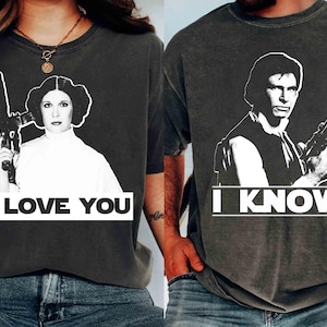 Può includere: Due magliette grigio scuro con immagini in bianco e nero di personaggi di un film di fantascienza. Una maglietta mostra una donna con la scritta "I LOVE YOU", l'altra un uomo con la scritta "I KNOW".