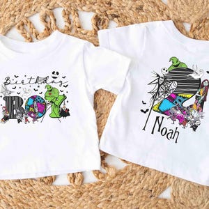 May include: Two white t-shirts with Halloween-themed graphics. One shirt says "Birthday Boy" with a colorful design featuring characters. The other shirt has the name "Noah" and a similar design with characters and a striped background.