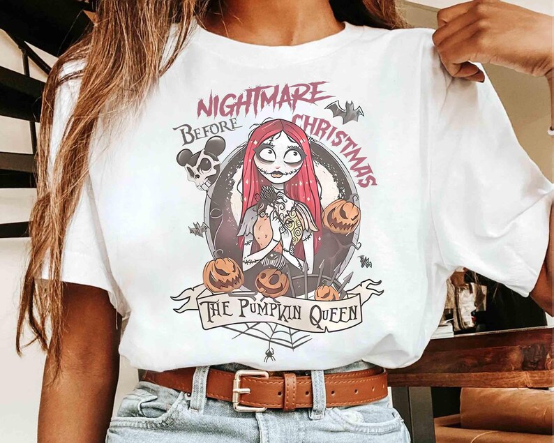 Puede incluir: Camiseta blanca con un dise&ntilde;o gr&aacute;fico de "Pesadilla antes de Navidad". El dise&ntilde;o incluye a Sally, calabazas, murci&eacute;lagos y el texto "Nightmare Before Christmas" y "The Pumpkin Queen".