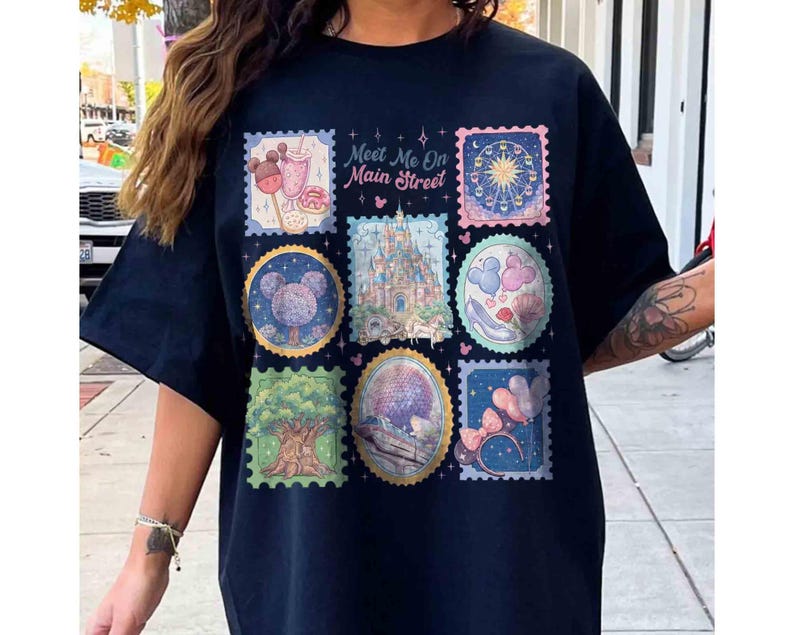 Peut inclure: Un t-shirt bleu marine avec un graphisme color&eacute; d'illustrations de style timbre-poste. Les timbres repr&eacute;sentent diverses ic&ocirc;nes de parc &agrave; th&egrave;me, dont un ch&acirc;teau, une grande roue et un arbre. Le texte "Meet Me On Main Street" est imprim&eacute; au-dessus des timbres.