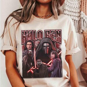 May include: A cream-coloured t-shirt with a graphic of Kylo Ren from Star Wars. The design includes the text "KYLO REN" in a distressed, red font, and images of Kylo Ren and other characters with red lightsabers.
