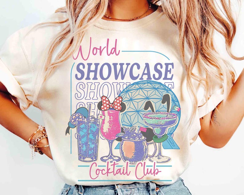 以下が含まれることがあります： 「World Showcase Cocktail Club」の文字とカクテルのイラストが描かれたクリーム色のTシャツ。幾何学的な球体と青、ピンク、紫の色使いが特徴で、楽しくカラフルなグラフィックです。