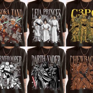 Puede incluir: Seis camisetas negras con personajes de Star Wars. Cada camiseta muestra un diseño diferente: Ahsoka Tano, Leia Princesa, C3PO, Stormtrooper, Darth Vader y Chewbacca. Los diseños son de estilo vintage, con ilustraciones y texto.