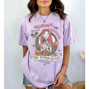 Puede incluir: Camiseta lila claro con un dise&ntilde;o gr&aacute;fico de "Pesadilla antes de Navidad". El dise&ntilde;o incluye a Sally, calabazas y el texto "The Pumpkin Queen". La camiseta tiene mangas cortas y cuello redondo.