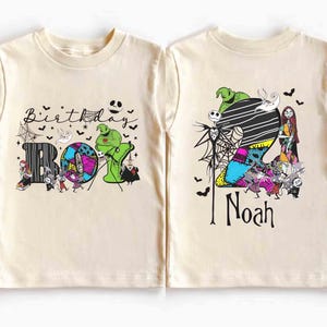 May include: A light beige short-sleeved t-shirt featuring a colorful graphic design. The front of the shirt says "Birthday Boy" with Halloween-themed characters. The back of the shirt has the name "Noah" and more Halloween characters.