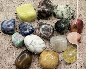 Puede incluir: Una colección de 14 piedras pulidas en varios colores y patrones, incluyendo verde, azul, rosa, blanco, marrón y amarillo. Las piedras están dispuestas en un círculo sobre una superficie marrón claro.