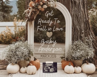 Könnte beinhalten: Eine Schwangerschaftsankündigung mit einem weißen, bogenförmigen Rahmen, verziert mit Blumen und dem Text "Get Ready To Fall in Love Baby Anderson March 2026." Kürbisse und ein Ultraschallbild sind zu sehen.