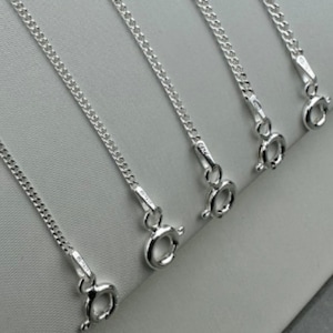 May include: Five silver chains with lobster claw clasps. The chains are all the same length and are arranged in a row.
