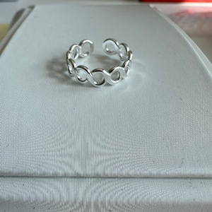 Puede incluir: Un anillo de plata con un diseño de cadena. El anillo está hecho de círculos entrelazados.